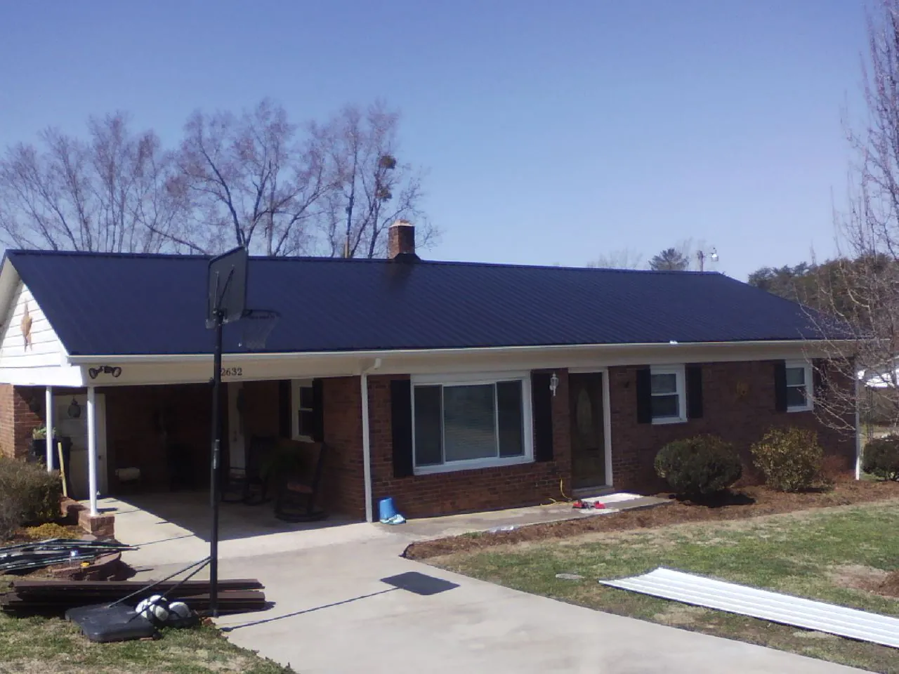 Finished dark blue metal roof on a brick ranch with a carport in Waterville
