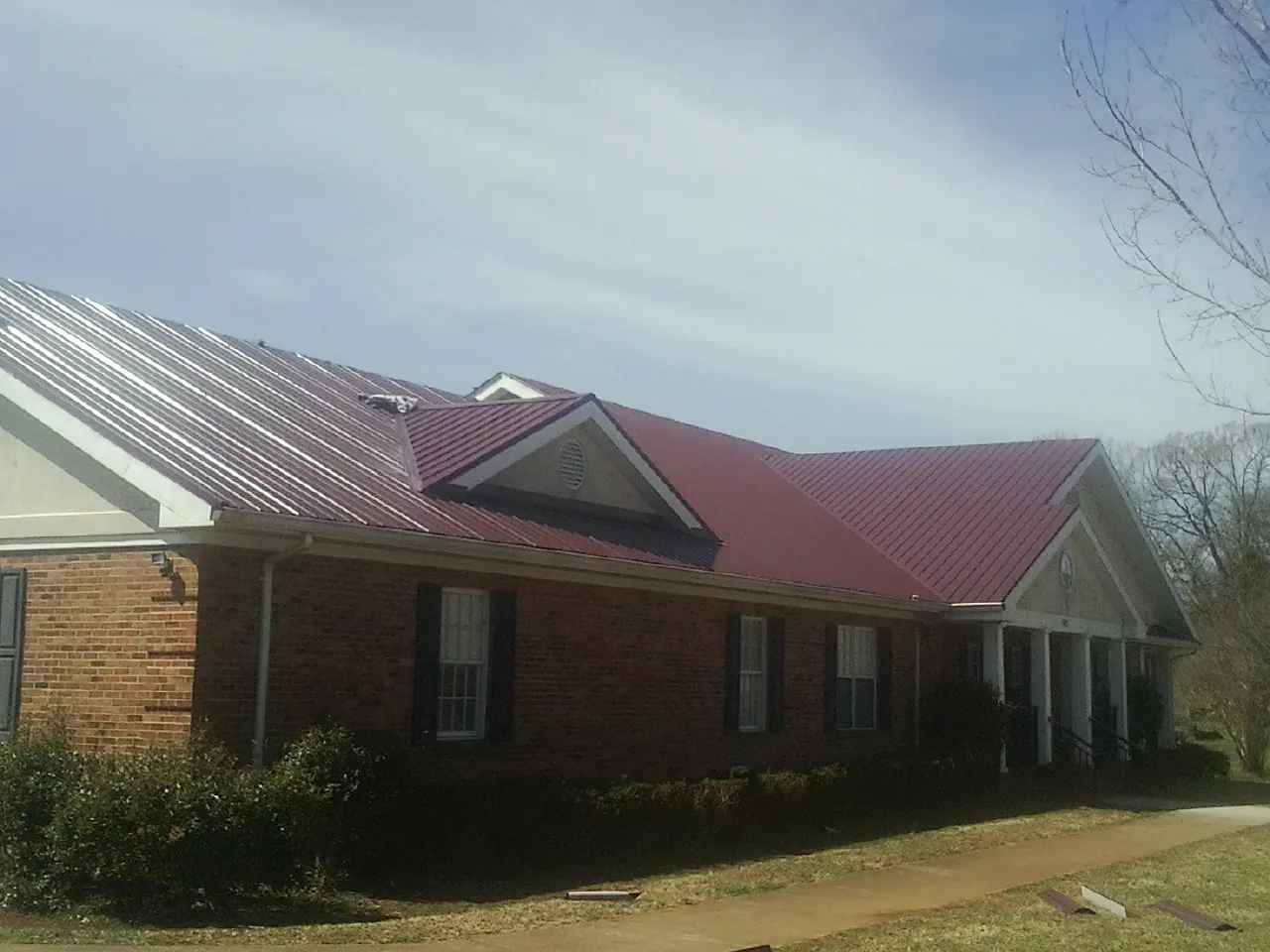 Red metal roof with gabled entries on a long brick building, from a Hail Damage Roof Repair job in Waterville